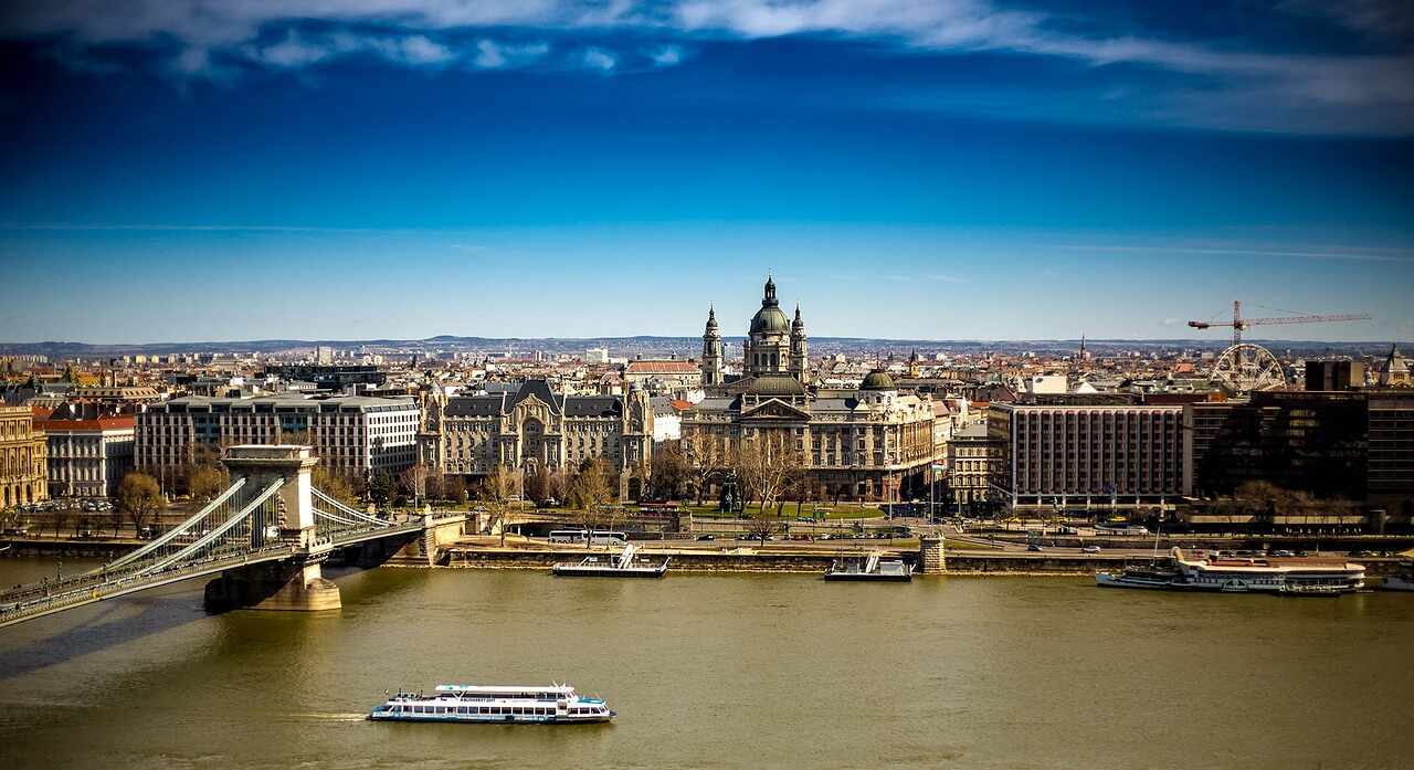 View of St. Stephen’s Basilica and the Budapest skyline from across the Danube River, with the Chain Bridge and sightseeing boats in the foreground