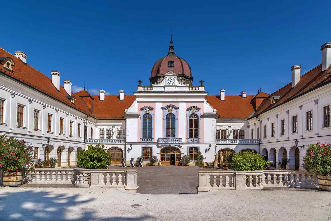 Exterior courtyard of the Royal Palace of Gödöllő under a blue sky, representing an important historical day trip destination near Budapest.